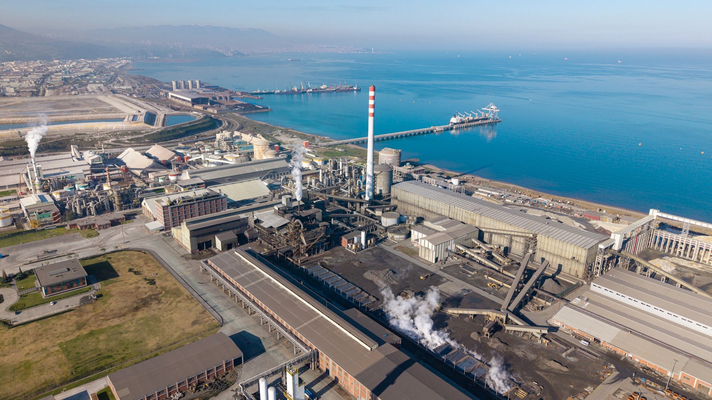 Large coastal industrial facility with smokestacks and port infrastructure
